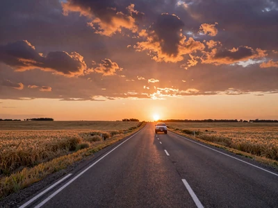 Pickup truck driving down a long rural highway through wheat fields at sunset - long distance rural dating